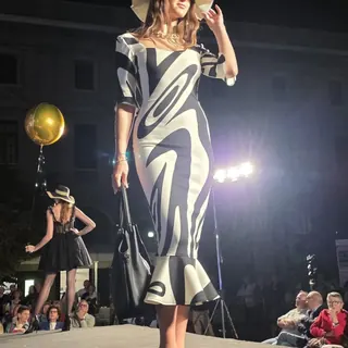 Modella in abito a sirena con stampa astratta bianca e nera, cappello e borsa, sulla passerella serale di Arte nella Moda